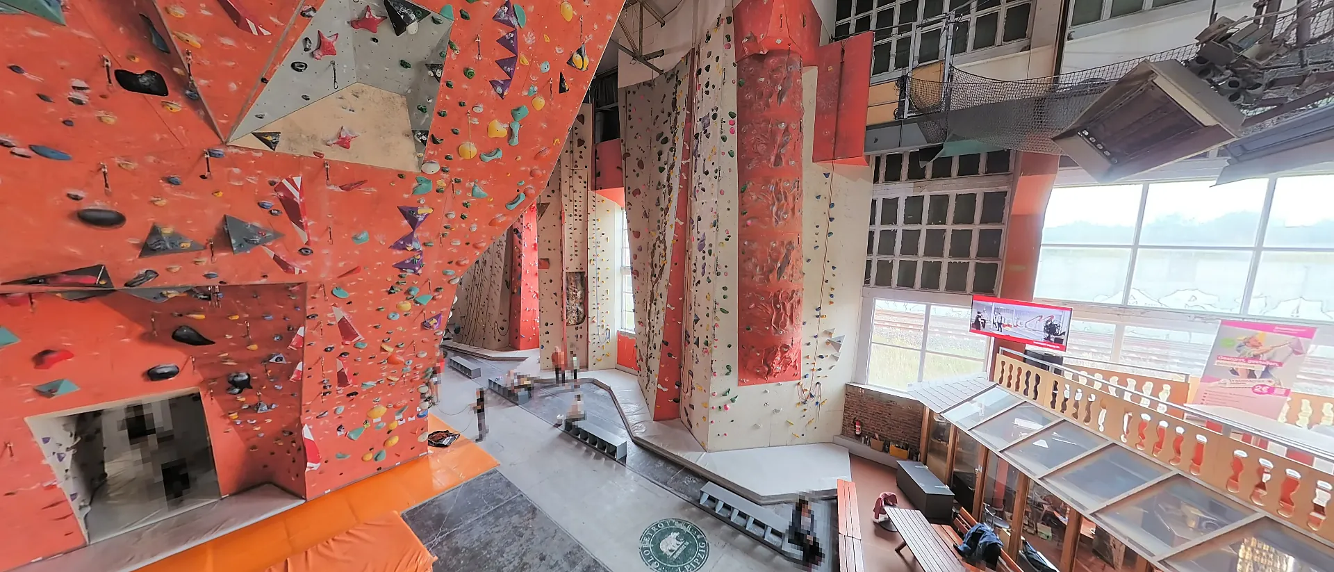 Haupthalle der Kletterhalle NO LIMIT: orangerote Kletterwände über zwei Etagen, rechts eine Empore mit Sitzbereich, hinten Fensterfront